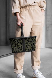 Person hält einen kleinen, stilvollen Einkaufskorb mit Leopardenmuster in der Hand, seitliche Perspektive.