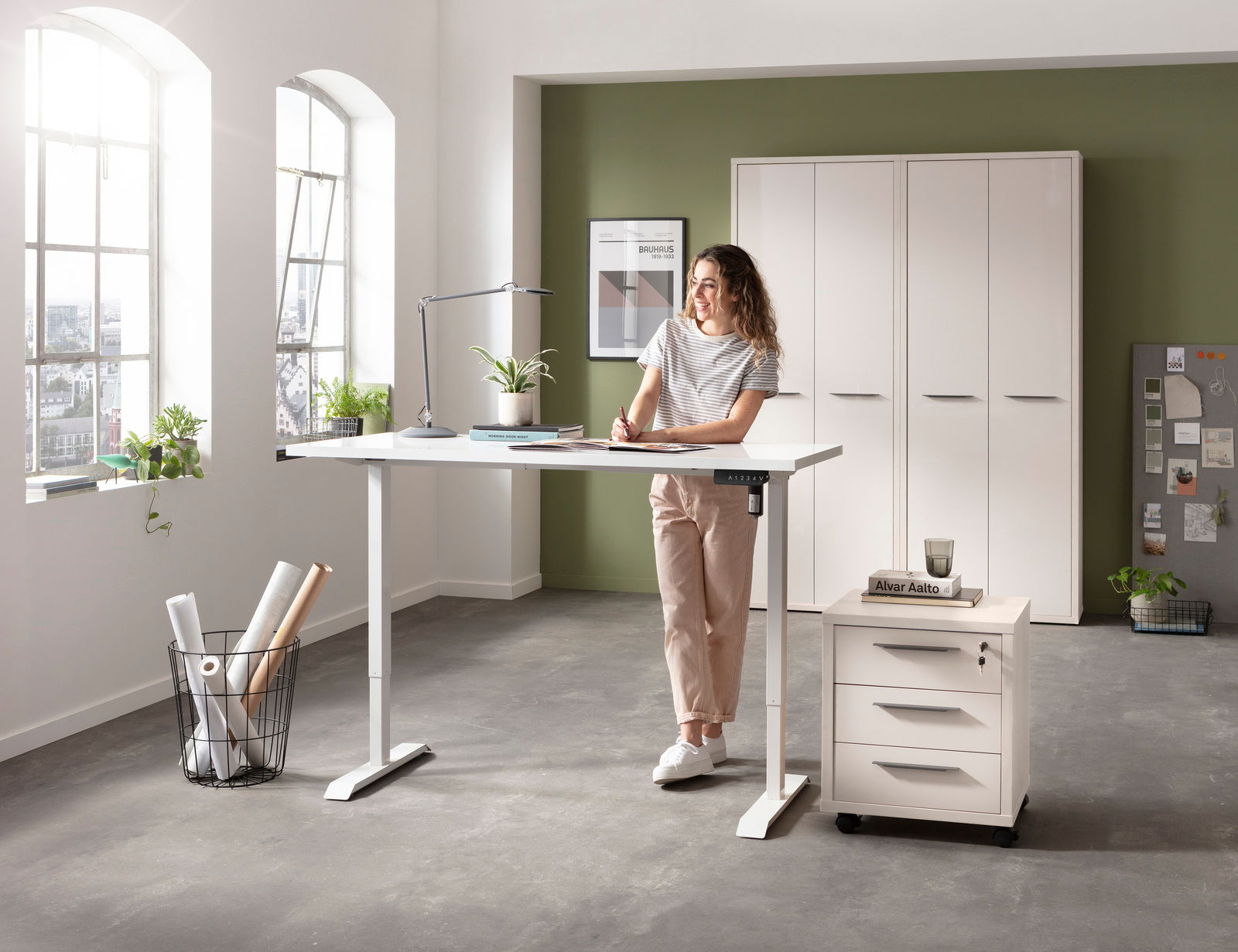 Elektrisch höhenverstellbarer Schreibtisch in einem modernen Büro mit einer Frau, die daran arbeitet. Perspektive von vorne.