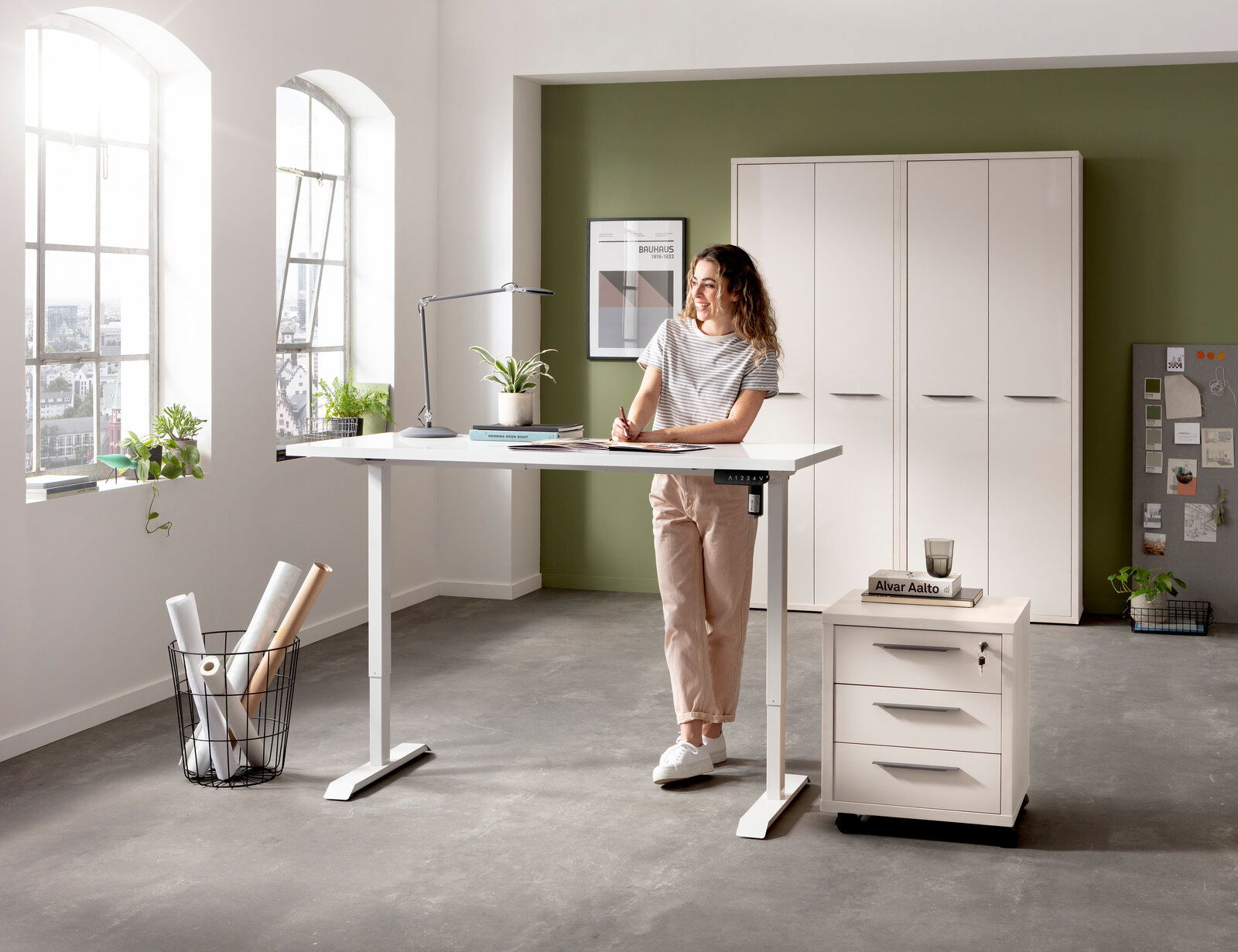 Elektrisch höhenverstellbarer Schreibtisch in einem modernen Büro mit einer Frau, die daran arbeitet. Perspektive von vorne.