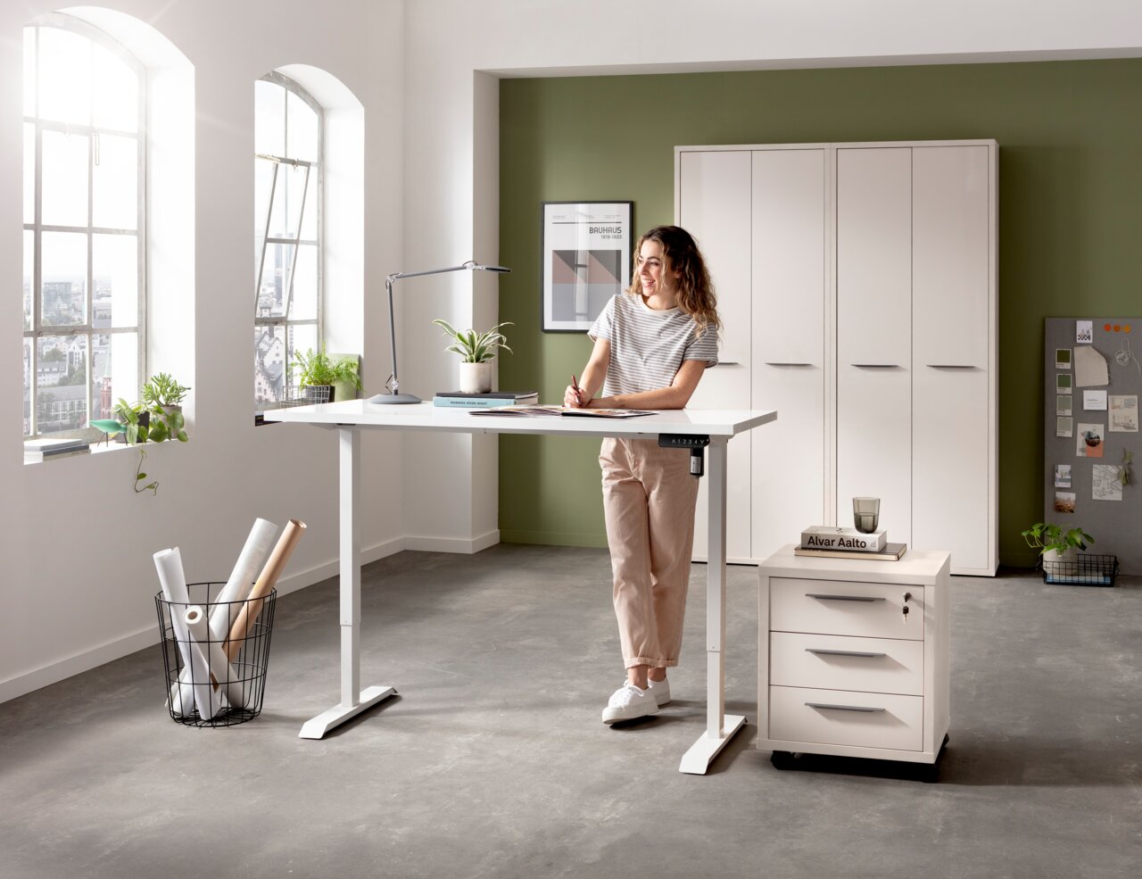Elektrisch höhenverstellbarer Schreibtisch in einem modernen Büro mit einer Frau, die daran arbeitet. Perspektive von vorne.