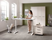 Elektrisch höhenverstellbarer Schreibtisch in einem modernen Büro mit einer Frau, die daran arbeitet. Perspektive von vorne.