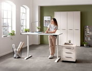 Elektrisch höhenverstellbarer Schreibtisch in einem modernen Büro mit einer Frau, die daran arbeitet. Perspektive von vorne.