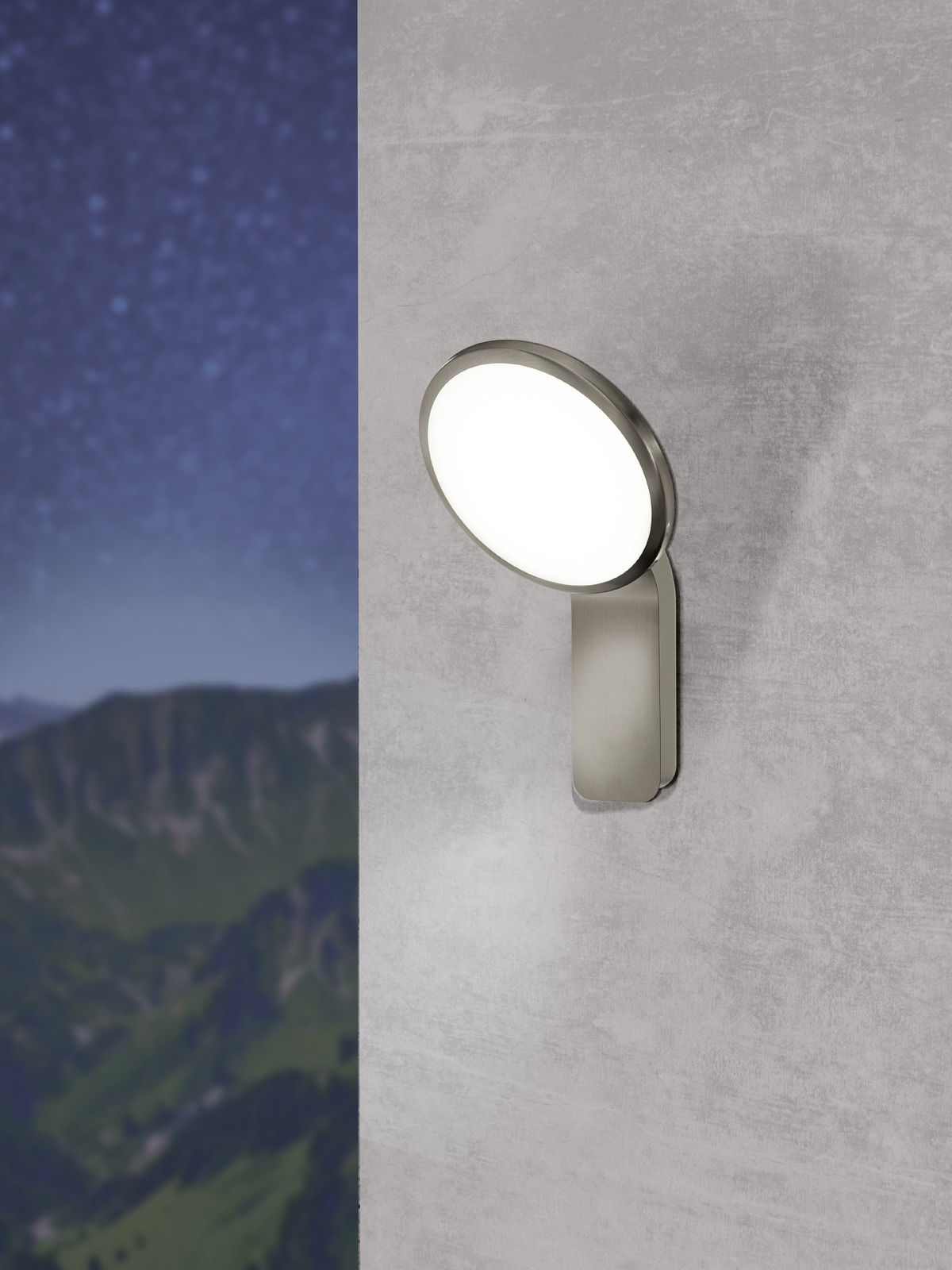 Moderne Außen-Wandleuchte Cicerone in seitlicher Perspektive an einer Wand montiert, mit leuchtendem, rundem Lampenschirm vor einem Hintergrund aus Bergen und Sternenhimmel.