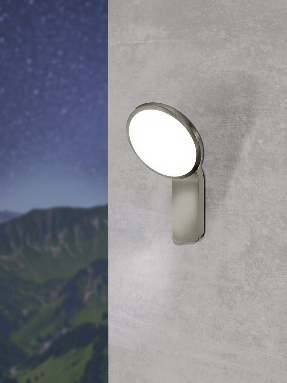 Moderne Außen-Wandleuchte Cicerone in seitlicher Perspektive an einer Wand montiert, mit leuchtendem, rundem Lampenschirm vor einem Hintergrund aus Bergen und Sternenhimmel.