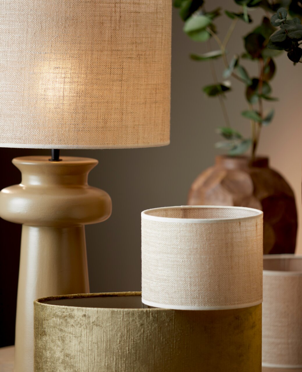 Cilindrische lampenkap in naturel beige, op de voorgrond op een tafel geplaatst, met een stijlvolle lamp en planten op de achtergrond.