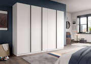 Moderner weißer Kleiderschrank mit fünf hohen Türen und schmalen schwarzen Griffleisten im Schlafzimmer, perspektivisch in leichter Schrägansicht von vorn links.