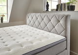 Boxspringbett mit gepolstertem Kopfteil in einem hellen Raum, seitliche Perspektive