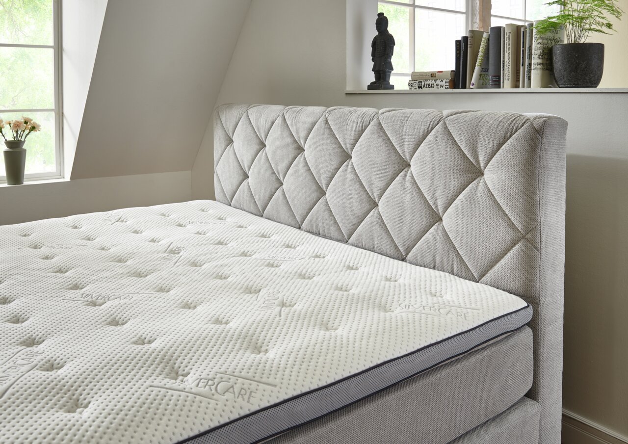 Boxspringbed met gestoffeerd hoofdeinde in een lichte kamer, zijaanzicht