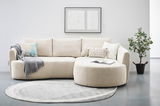 Beiges Ecksofa AVIANO mit Ottomane rechts, dekoriert mit Kissen und Decke, vor einem modernen Kunstwerk an der Wand. Perspektive: Frontalansicht.