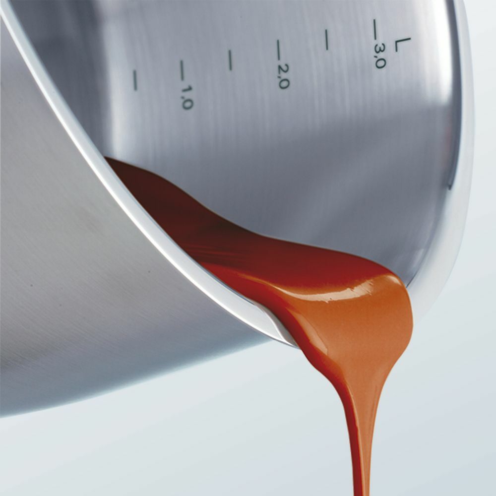 Nahaufnahme eines Topfes aus Edelstahl mit Skala, aus dem eine rote Flüssigkeit gegossen wird.