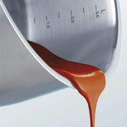 Nahaufnahme eines Topfes aus Edelstahl mit Skala, aus dem eine rote Flüssigkeit gegossen wird.