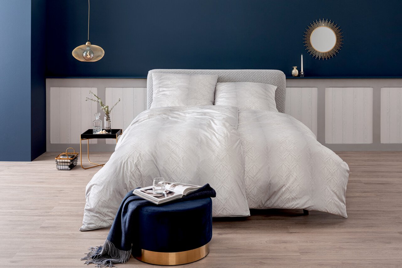 Elegante Bettwäsche in Weiß mit dezentem Muster, präsentiert in einem stilvoll eingerichteten Schlafzimmer mit blauer Wand und dekorativen Elementen, aus der Vorderansicht fotografiert.