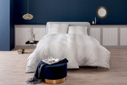 Elegante Bettwäsche in Weiß mit dezentem Muster, präsentiert in einem stilvoll eingerichteten Schlafzimmer mit blauer Wand und dekorativen Elementen, aus der Vorderansicht fotografiert.