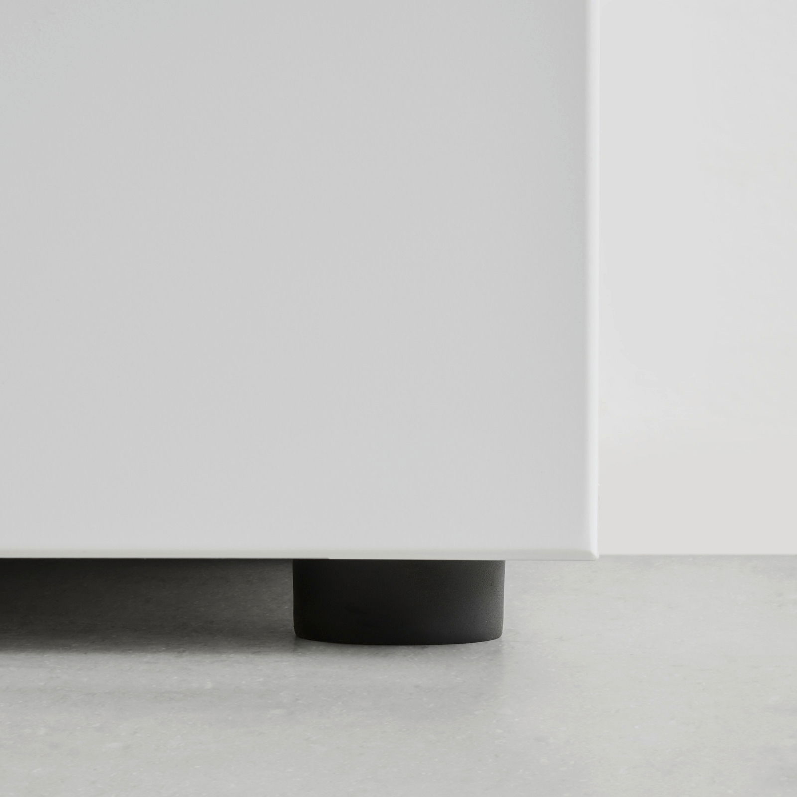 Nahaufnahme der unteren Ecke eines weißen Garderobenschranks mit schwarzem Fuß auf grauem Boden.