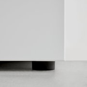 Nahaufnahme der unteren Ecke eines weißen Garderobenschranks mit schwarzem Fuß auf grauem Boden.