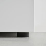 Nahaufnahme der unteren Ecke eines weißen Garderobenschranks mit schwarzem Fuß auf grauem Boden.