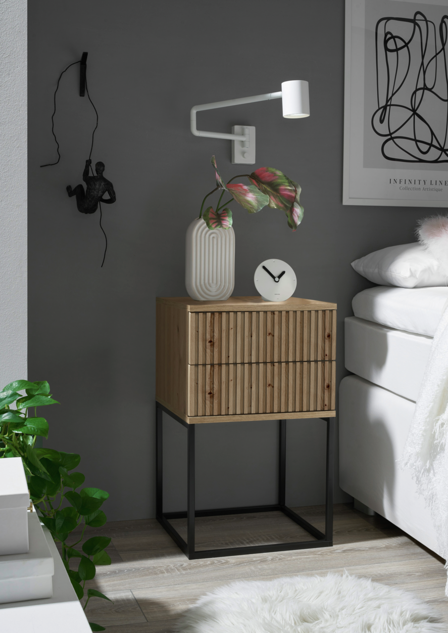 Moderne Nachtkommode aus Holz mit gerillter Front und schwarzem Metallgestell, seitliche Perspektive, dekoriert mit einer Vase und einer Uhr.