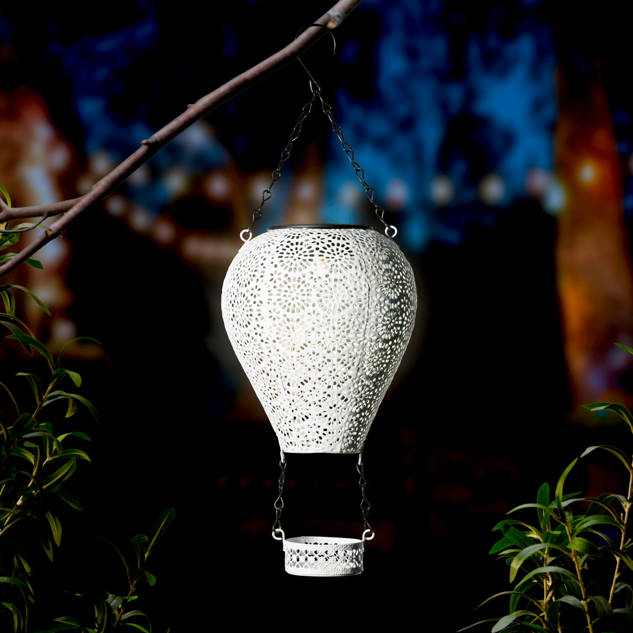 Metallischer Solarballon in Form eines Heißluftballons, aufgehängt an einem Ast, mit filigranem Muster und leuchtendem Inneren, seitliche Perspektive.