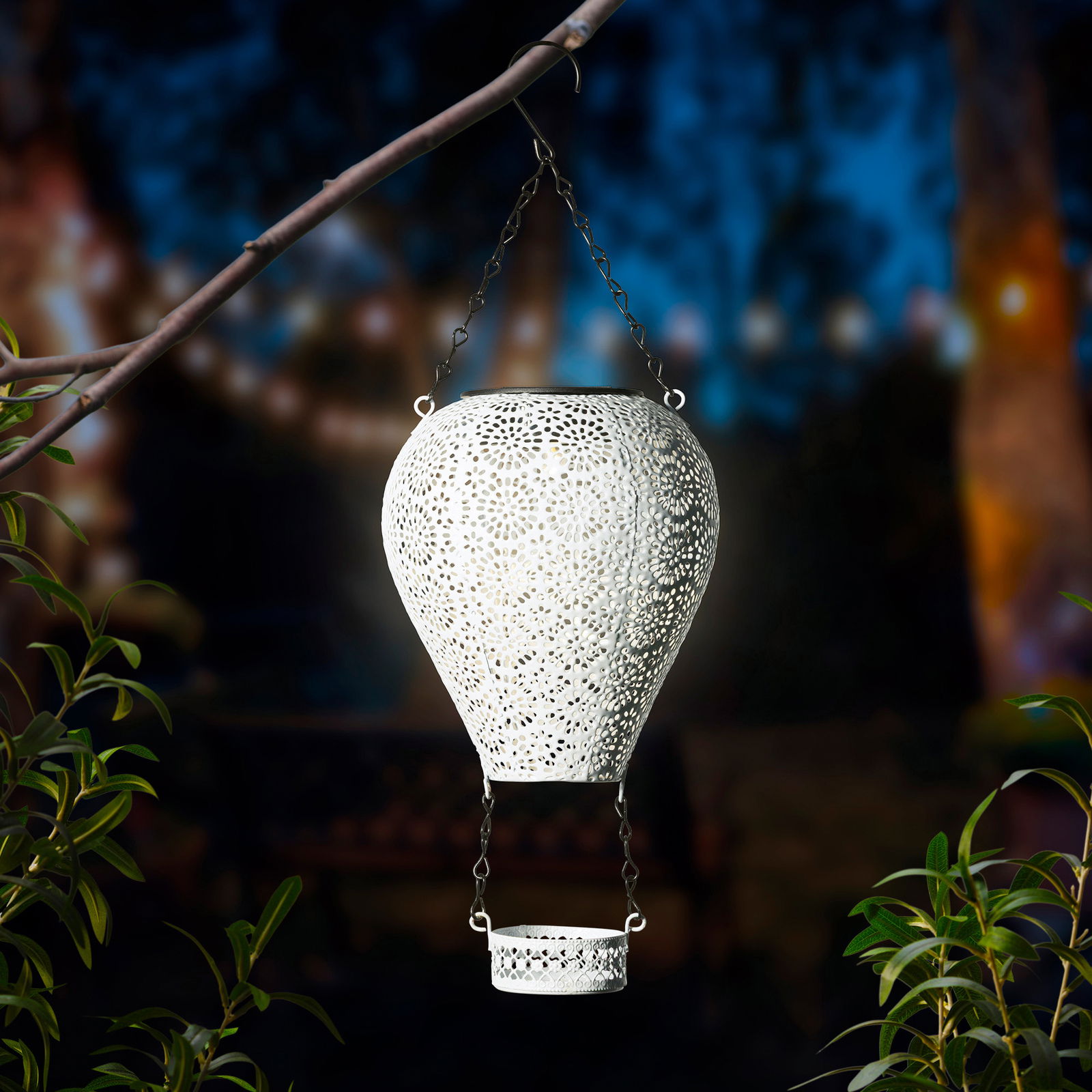 Metallischer Solarballon in Form eines Heißluftballons, aufgehängt an einem Ast, mit filigranem Muster und leuchtendem Inneren, seitliche Perspektive.