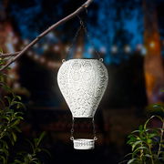 Metallischer Solarballon in Form eines Heißluftballons, aufgehängt an einem Ast, mit filigranem Muster und leuchtendem Inneren, seitliche Perspektive.