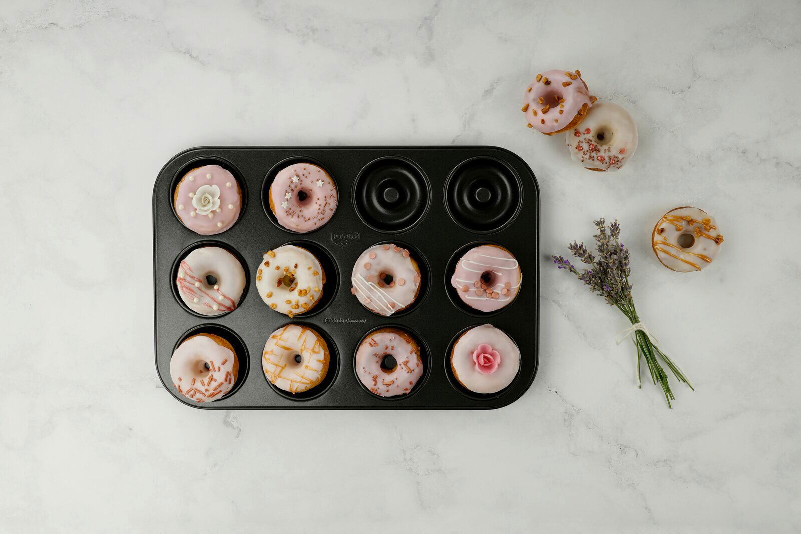 Dr. Oetker Donutbackform TRADITION Donutbackform mit zwölf Donuts, dekoriert mit rosa und weißem Zuckerguss, aus der Vogelperspektive fotografiert.