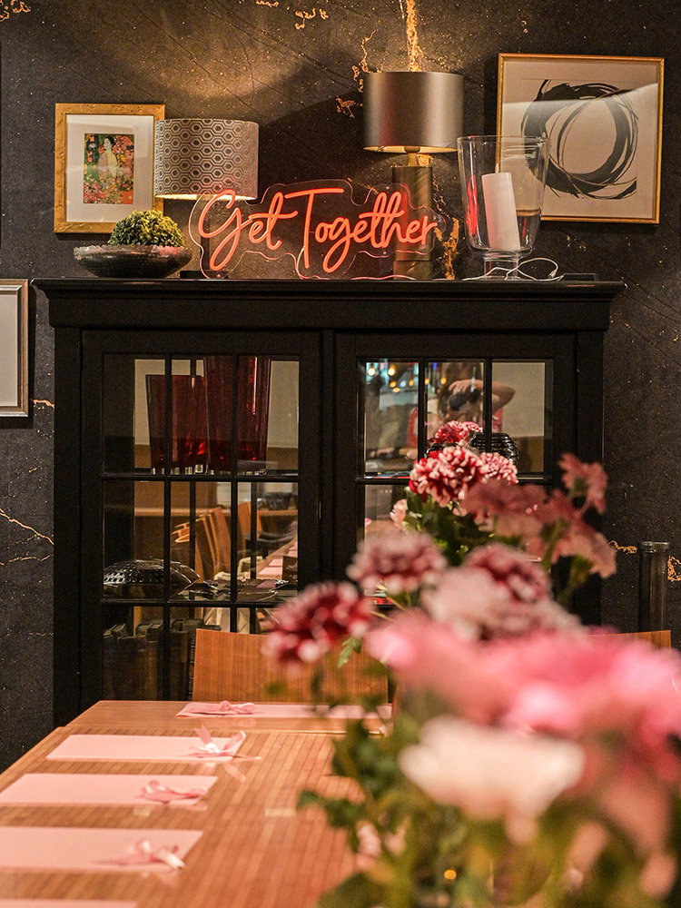 Stijlvol ingerichte eventlocatie met verlichte ‘Get Together’-letters, bloemendecoratie en een feestelijk gedekte tafel in warme roze tinten.