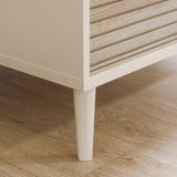 Nahaufnahme der unteren Ecke eines Kleiderschranks mit Holzoptik und weißen Beinen, auf einem Holzboden stehend.