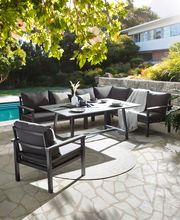 Lounge-Set im Garten mit Blick auf einen Pool, bestehend aus einem Ecksofa, einem Tisch und einem Sessel, umgeben von grüner Natur.