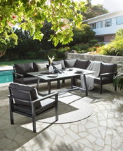 Loungeset in de tuin met uitzicht op een zwembad, bestaande uit een hoekbank, een tafel en een fauteuil, omgeven door weelderig groen.