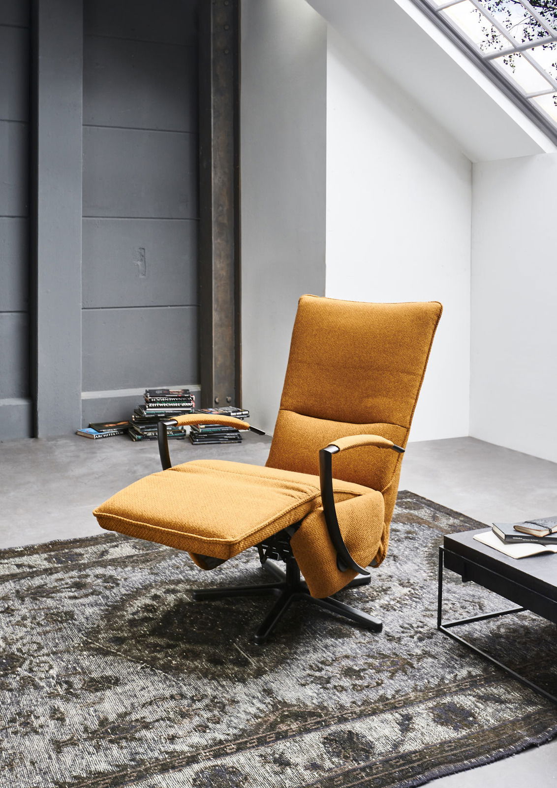 Moderner, drehbarer Relaxsessel in senfgelber Farbe mit ausgeklapptem Fußteil, seitliche Perspektive in einem stilvollen Wohnzimmer.