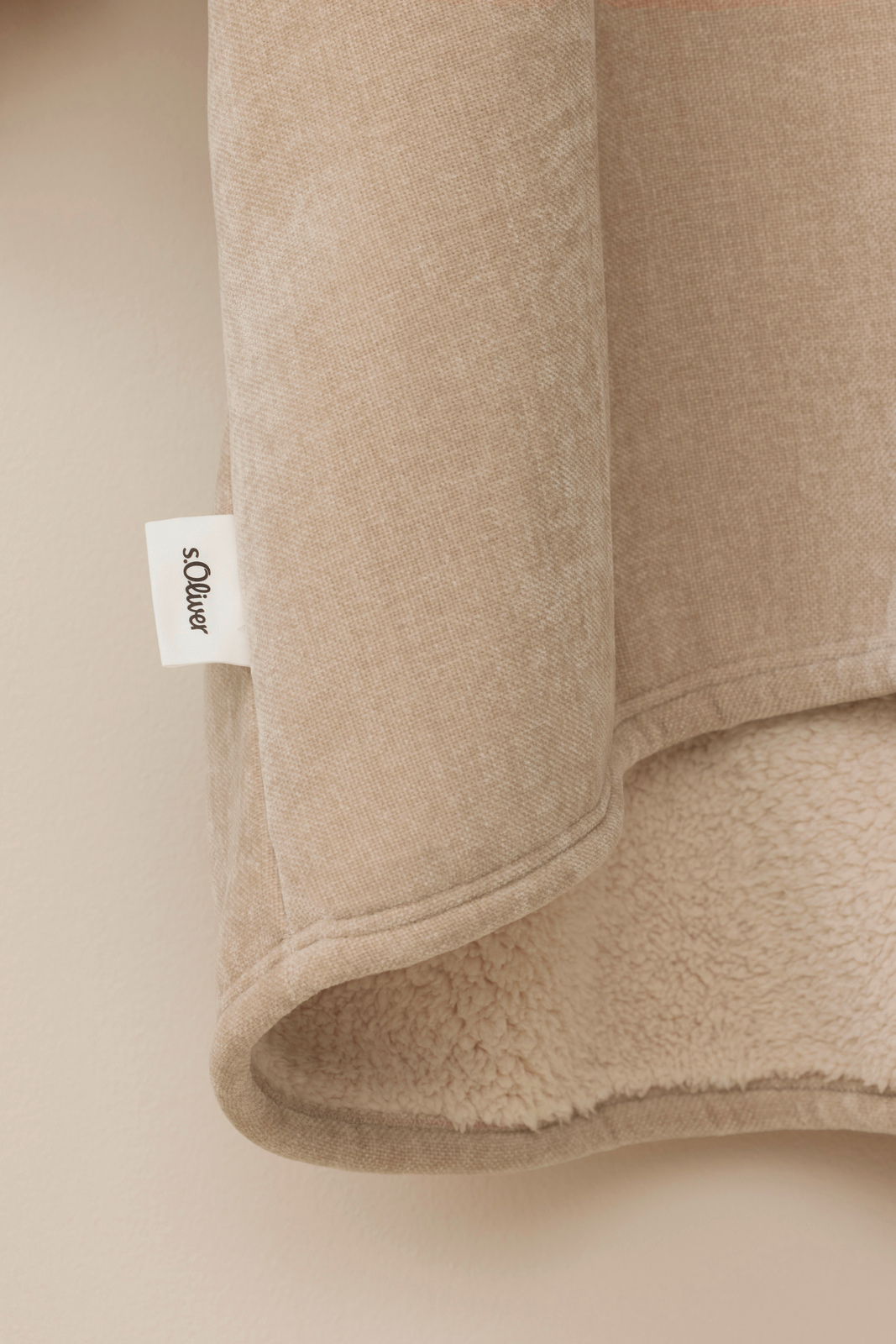 Nahaufnahme eines beigen Lounge Hoodies mit weichem Futter und sichtbarem Markenetikett, seitliche Perspektive.