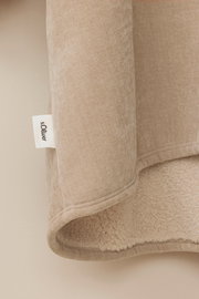 Nahaufnahme eines beigen Lounge Hoodies mit weichem Futter und sichtbarem Markenetikett, seitliche Perspektive.