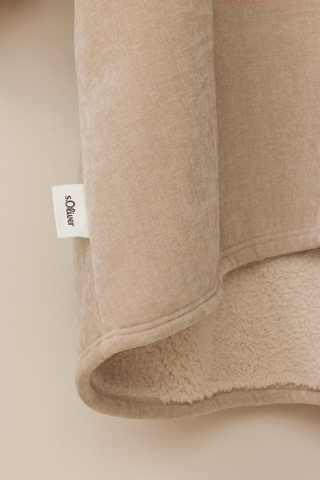 Nahaufnahme eines beigen Lounge Hoodies mit weichem Futter und sichtbarem Markenetikett, seitliche Perspektive.