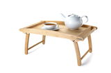 Holz-Betttablett mit hochgeklappten Beinen, darauf eine weiße Teekanne und Tasse, seitliche Perspektive