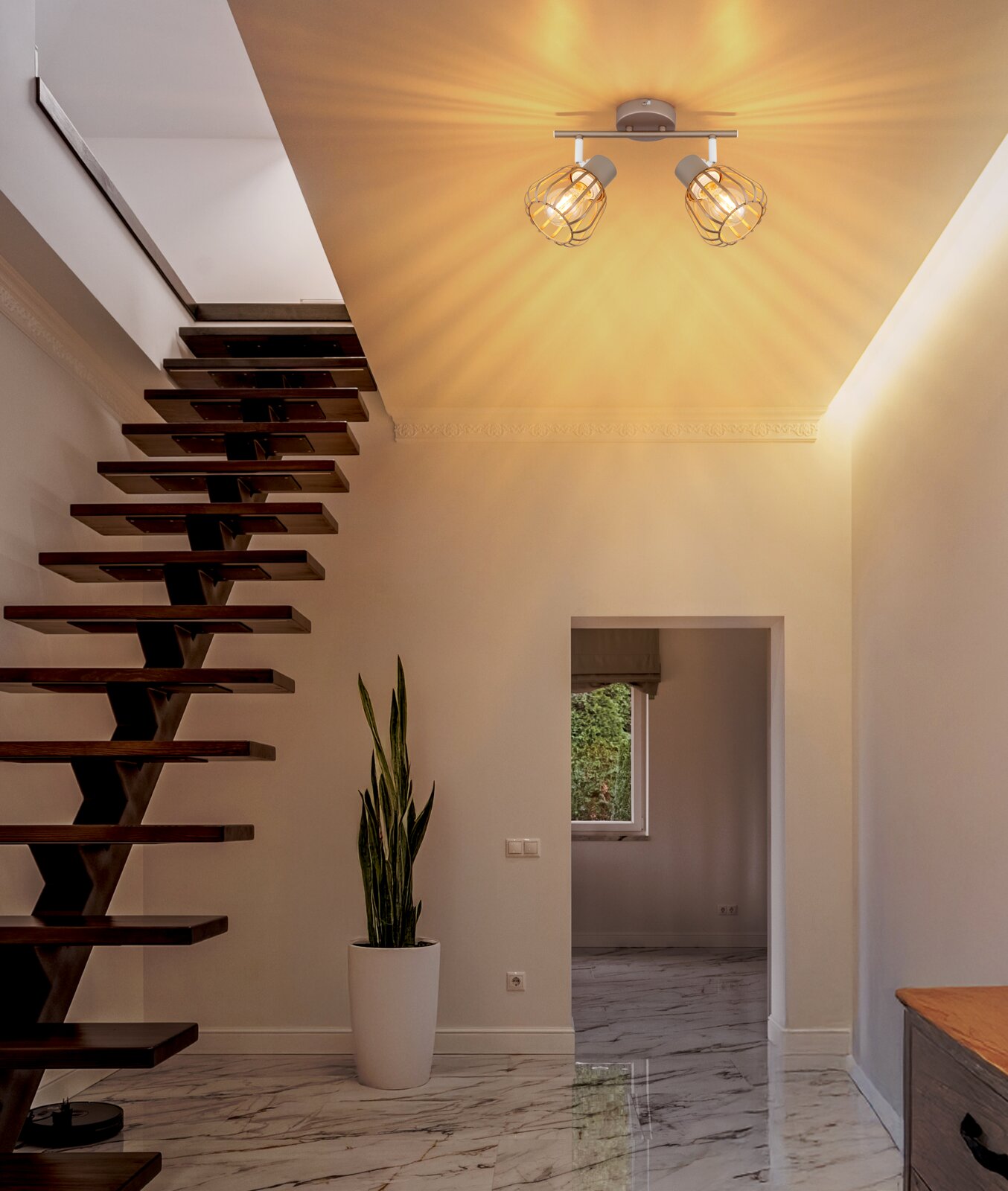 Moderne Deckenleuchte mit zwei verstellbaren Spotköpfen und goldfarbenen Drahtschirm-Käfigen, warm leuchtend im Flur über einer Holztreppe, fotografiert aus leichtem Untersichtwinkel zur Decke