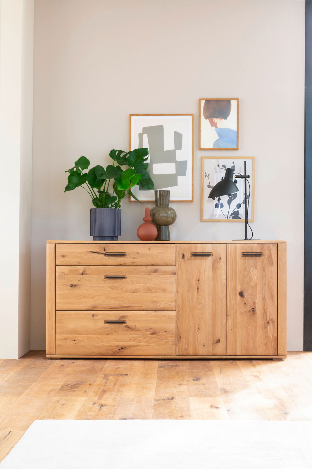 Cantus Sideboard ASINARA Holz-Sideboard mit drei Schubladen und zwei Türen, dekoriert mit Pflanzen und Kunstwerken, aus frontaler Perspektive.