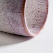 Nahaufnahme aus schräger Seitenperspektive auf den abgerundeten Rand einer glänzenden Keramikschale in Weiß mit roséfarbenen Sprenkeln auf hellem Hintergrund.