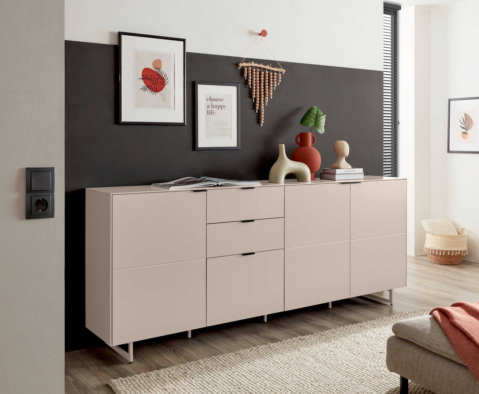 Modernes Sideboard in Greige/Beige mit drei Türen und zwei Schubladen auf schlanken Metallfüßen, dekoriert mit Vasen und Bildern, in schräger Frontansicht im Wohnzimmer.