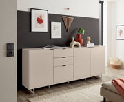 Modernes Sideboard in Greige/Beige mit drei Türen und zwei Schubladen auf schlanken Metallfüßen, dekoriert mit Vasen und Bildern, in schräger Frontansicht im Wohnzimmer.