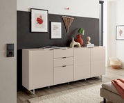 Modern dressoir in greige/beige met drie deuren en twee lades op slanke metalen poten, versierd met vazen en schilderijen, in schuin vooraanzicht in de woonkamer.