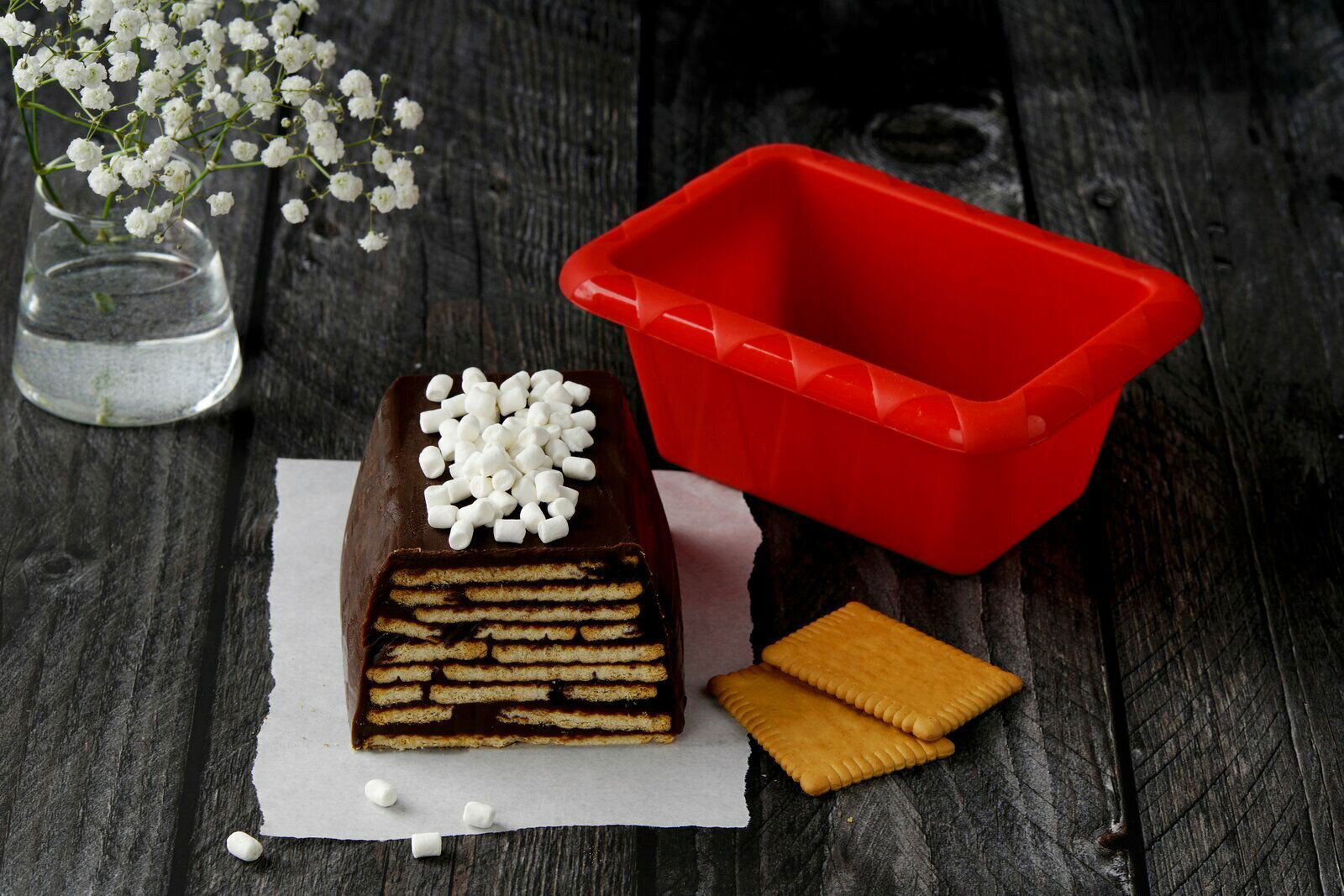 Rote Silikon-Kastenform neben einem Schichtkuchen mit Schokolade und Keksen, von oben fotografiert.