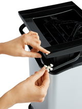 Nahaufnahme eines silbernen Treteimers Paso 40L mit geöffneter Klappe, in der eine Hand ein kleines weißes Teil einsetzt.