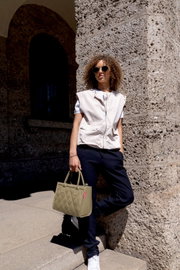 Frau mit Sonnenbrille lehnt an einer Steinwand und hält eine olivgrüne, gesteppte Handtasche in der Hand. Die Tasche ist im Vordergrund sichtbar.