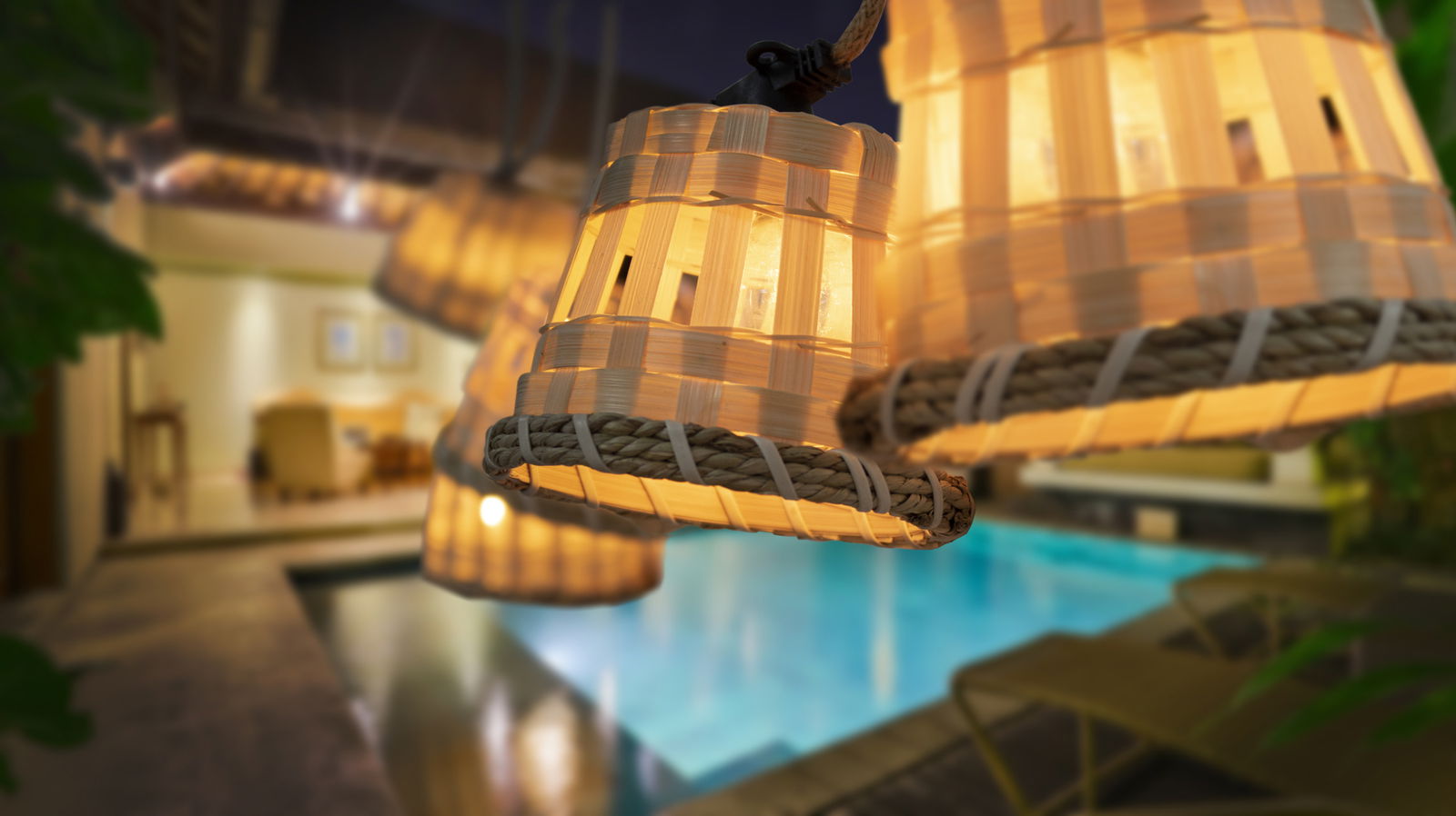 Nahaufnahme einer beleuchteten, geflochtenen Girlande mit warmem Licht, aufgehängt über einem Pool in einer abendlichen Außenumgebung.