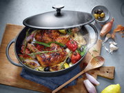 Gusseiserner Bräter mit Deckel, gefüllt mit gebratenem Hähnchen, Tomaten, Zwiebeln und Kräutern, aus der Vogelperspektive fotografiert.