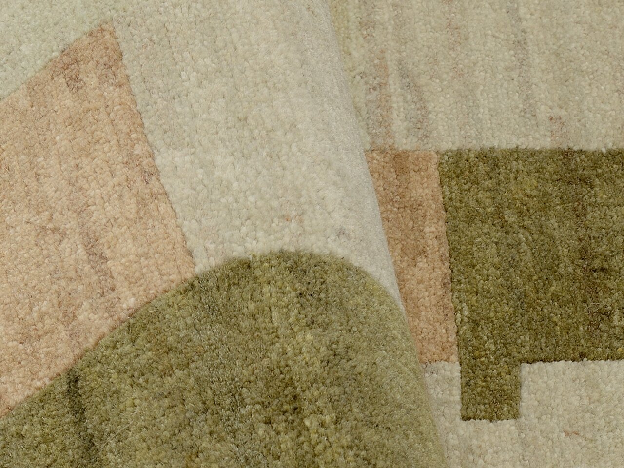 Nahaufnahme eines Wollteppichs mit geometrischem Muster in Beige- und Grüntönen, leicht gefaltet.