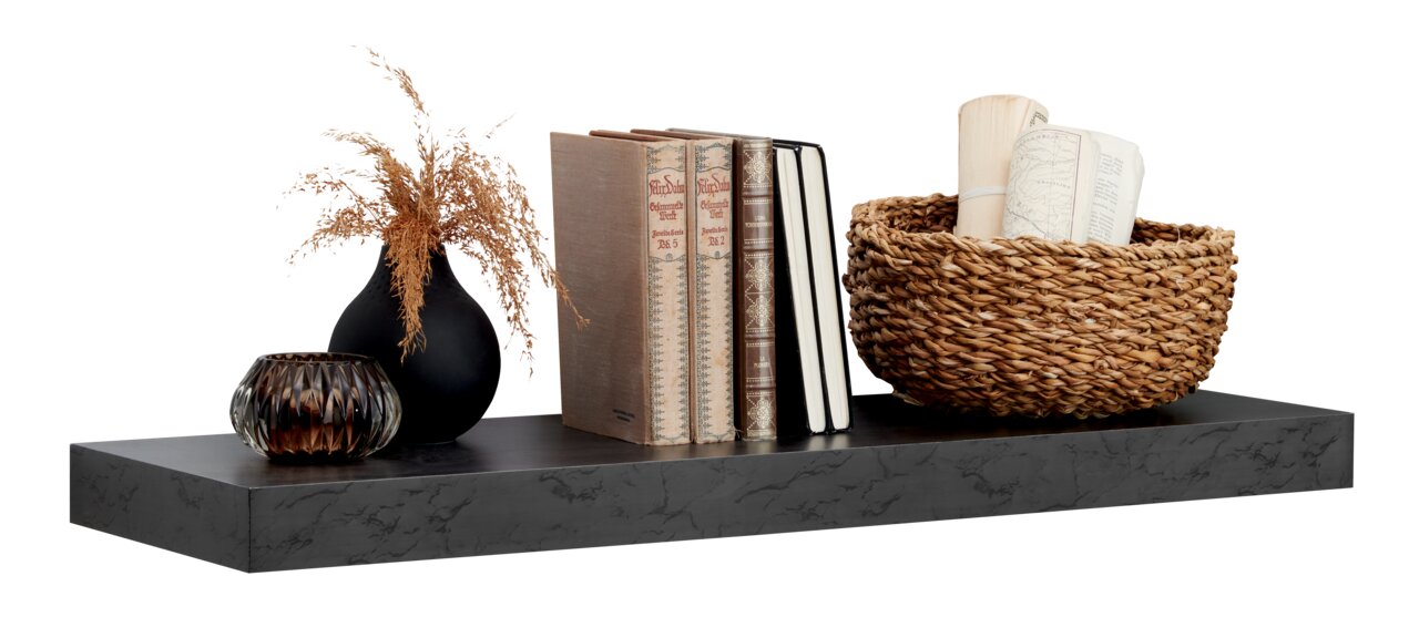 Schwarzes Wandboard mit Dekoration, darunter eine schwarze Vase mit getrockneten Gräsern, Bücher, ein Notizbuch und ein geflochtener Korb mit Papierrollen, seitliche Perspektive.