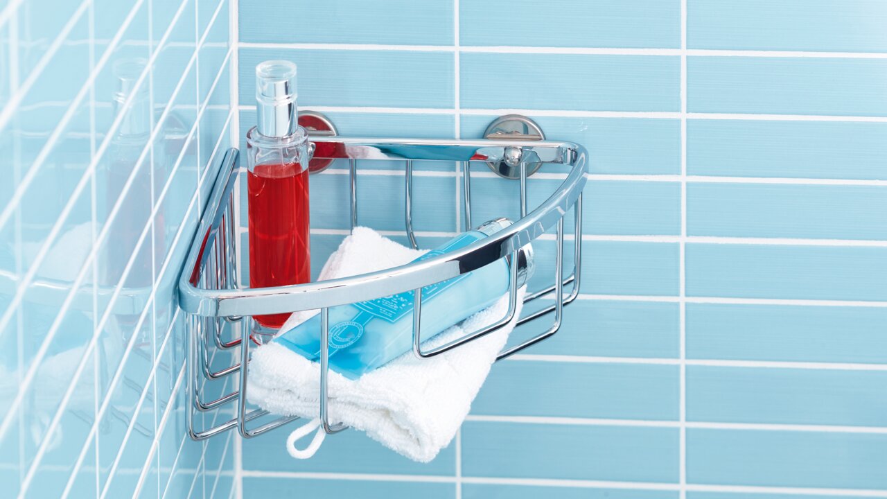 Eckduschkorb aus Chrom in einer blauen gefliesten Dusche, gefüllt mit einer roten Flasche, einem blauen Behälter und einem weißen Handtuch, von vorne betrachtet.