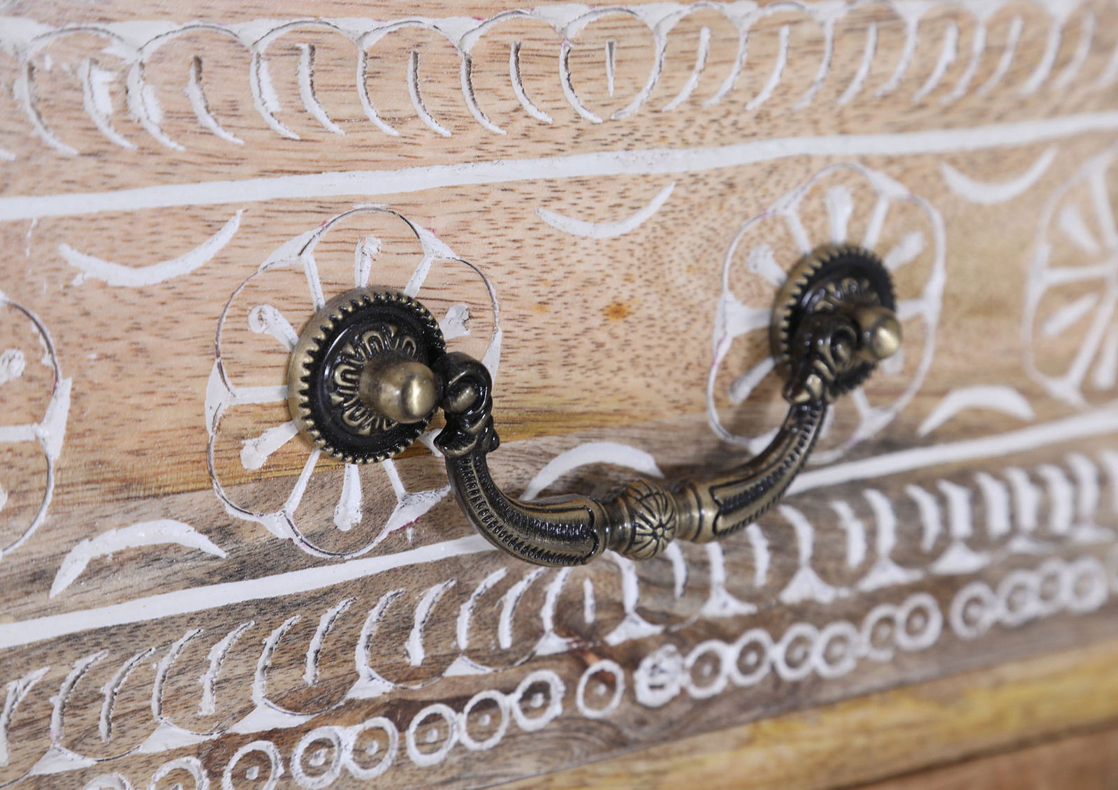 Nahaufnahme eines kunstvoll verzierten Schubladengriffs aus Metall auf einer Holzoberfläche mit geschnitzten Mustern.