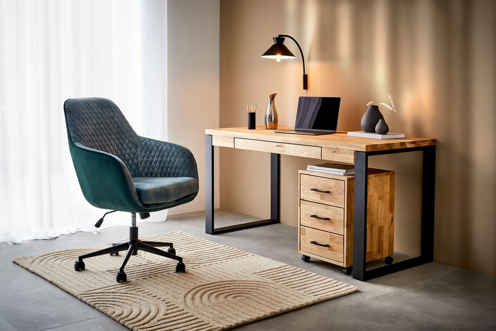 Moderner Schreibtisch aus Holz mit schwarzem Metallrahmen, seitlich betrachtet. Der Schreibtisch ist mit einer Lampe, einem Laptop und Dekorationen ausgestattet. Daneben steht ein gepolsterter Bürostuhl auf einem Teppich.